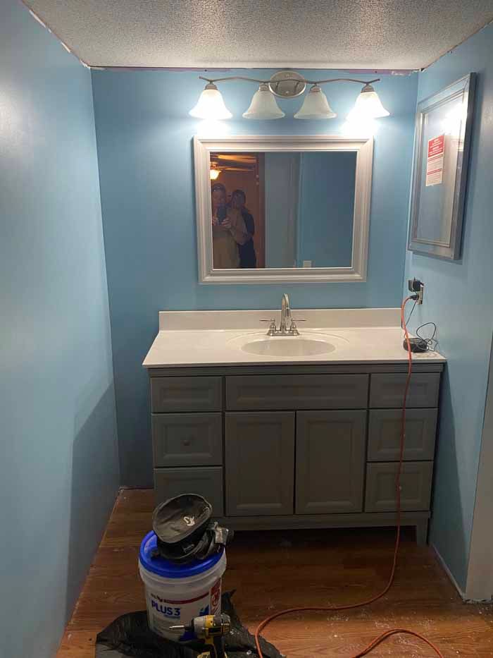 Bathroom vanity with mirror and three lights above, blue walls, and a bucket on the floor.