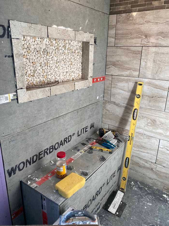 Construction site with WonderBoard panel, wall tile, tools, and a yellow level leaning against the wall