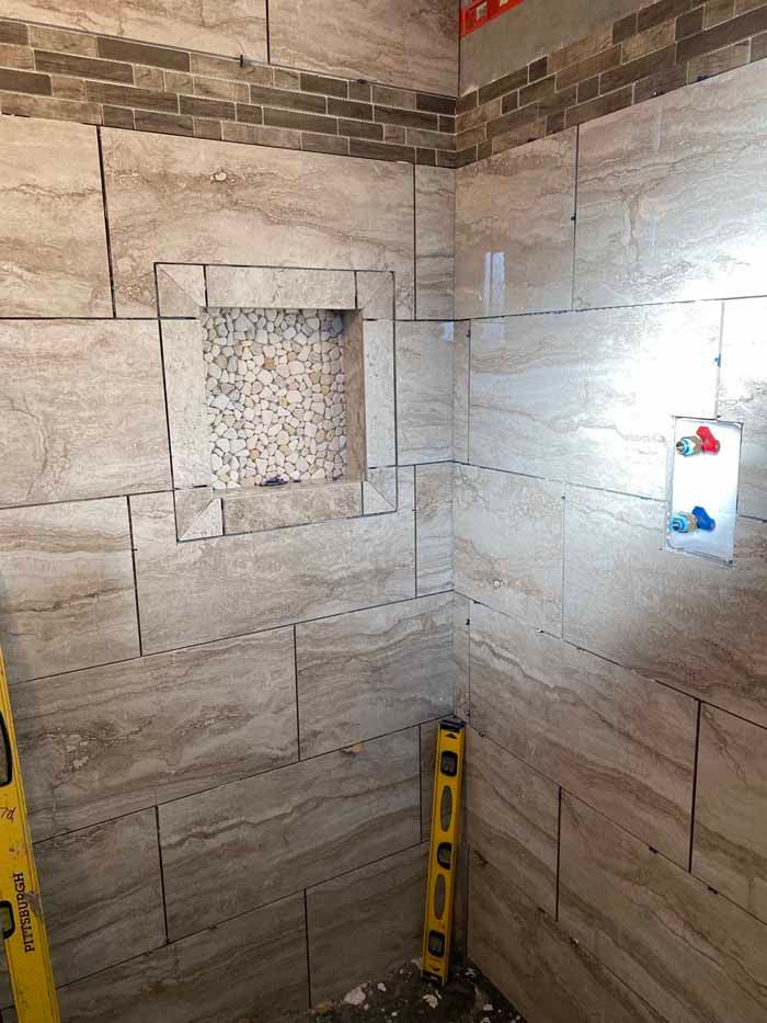 Partially tiled shower wall with a square recessed niche and a level on the floor