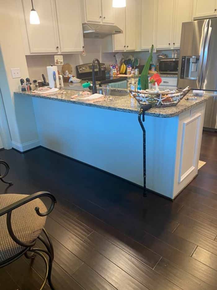 Modern kitchen with white cabinets, granite island, stainless fridge, and dark hardwood floors.