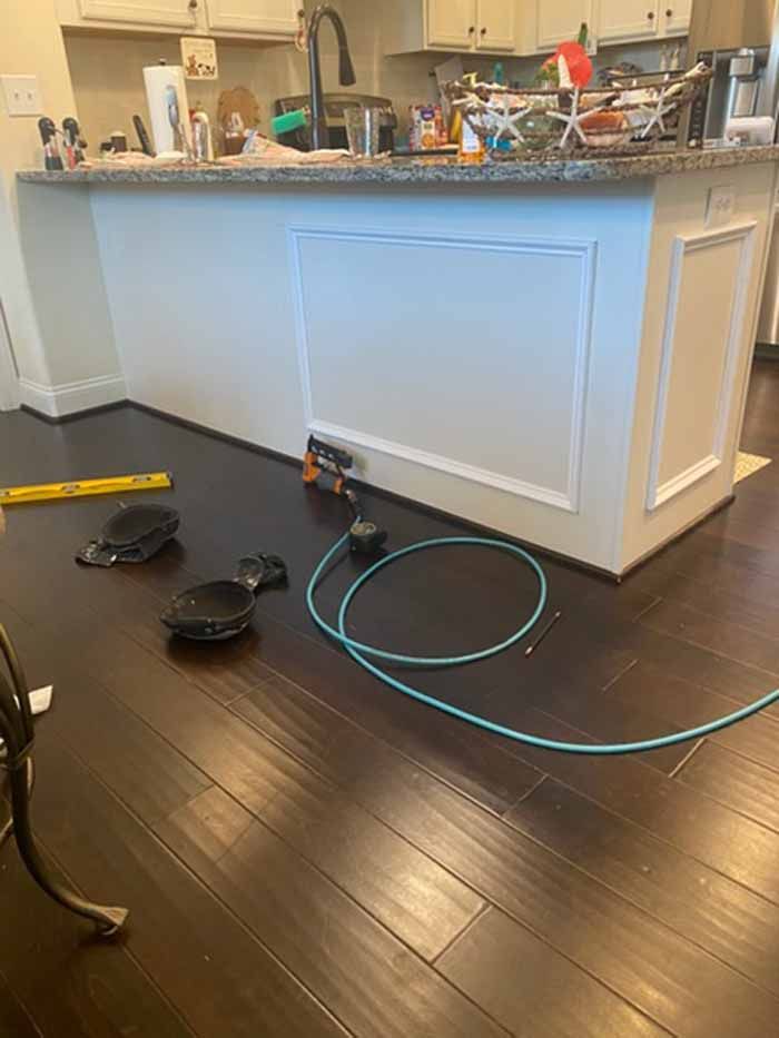 Kitchen island with a charger, tangled cables, and two robot vacuums on a hardwood floor
