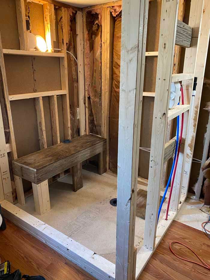 Unfinished bathroom framing with a built-in bench, exposed studs, and plumbing lines.