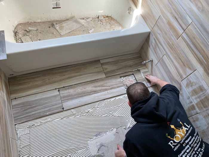 Worker installing wood-look tile flooring in a bathroom near a bathtub.