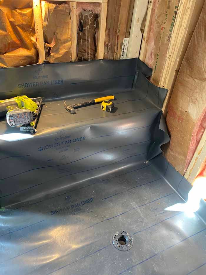 Bathroom under construction with black waterproofing membrane, insulation, and tools on the floor.