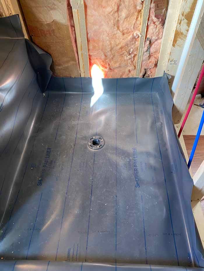 Black shower pan with center drain in a partially finished bathroom, with exposed wall framing.