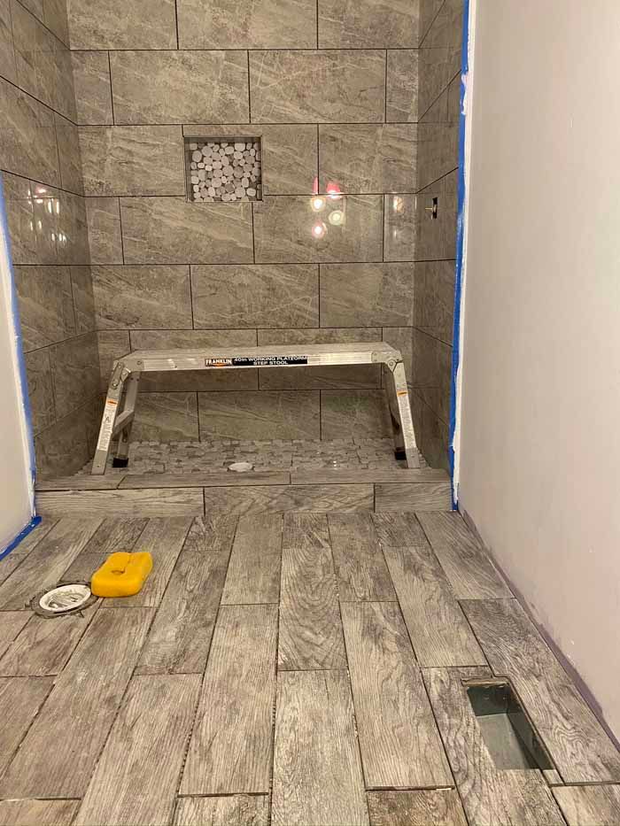 Bathroom shower under construction with tiled walls, floor, and a recessed niche.