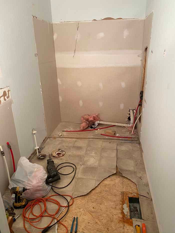 Small unfinished room under renovation with exposed walls, bare floor, tools, cords, and construction materials.