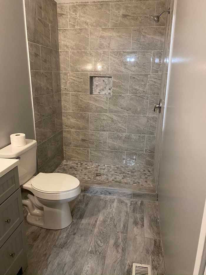 Small tiled bathroom with toilet, sink, walk-in shower, and gray floor tile.