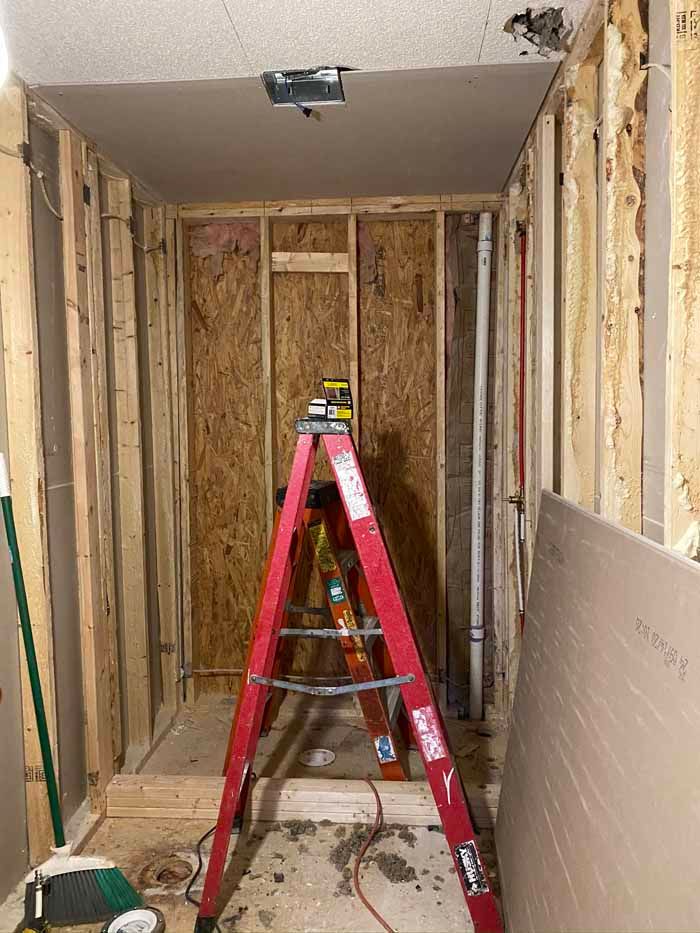 Partially gutted hallway with exposed studs, a red step ladder, and drywall in a renovation area