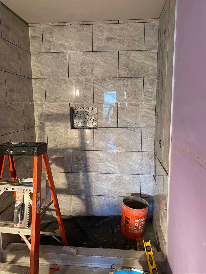 Bathroom shower under renovation with gray tile wall, step ladder, and orange bucket