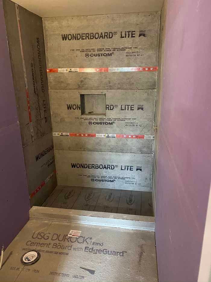 Partially tiled shower alcove with waterproof backer boards and red seam tape awaiting finish work