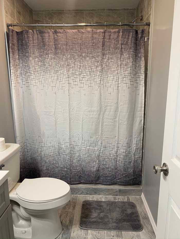 Small bathroom with a toilet, gray bath mat, and gradient shower curtain over a tub.