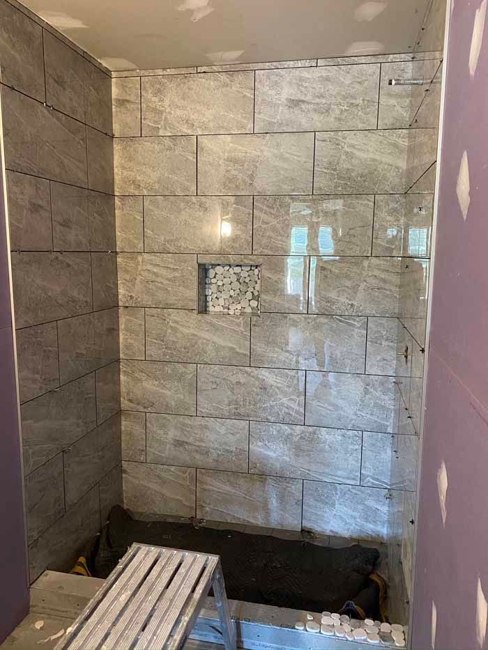 Bathroom shower under renovation with gray stone tile walls and a shower bench