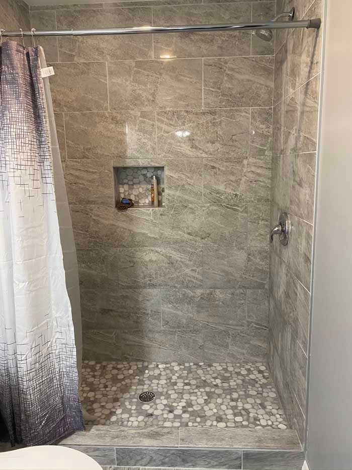 Stone-tiled shower stall with a curtain, small niche, and pebble floor