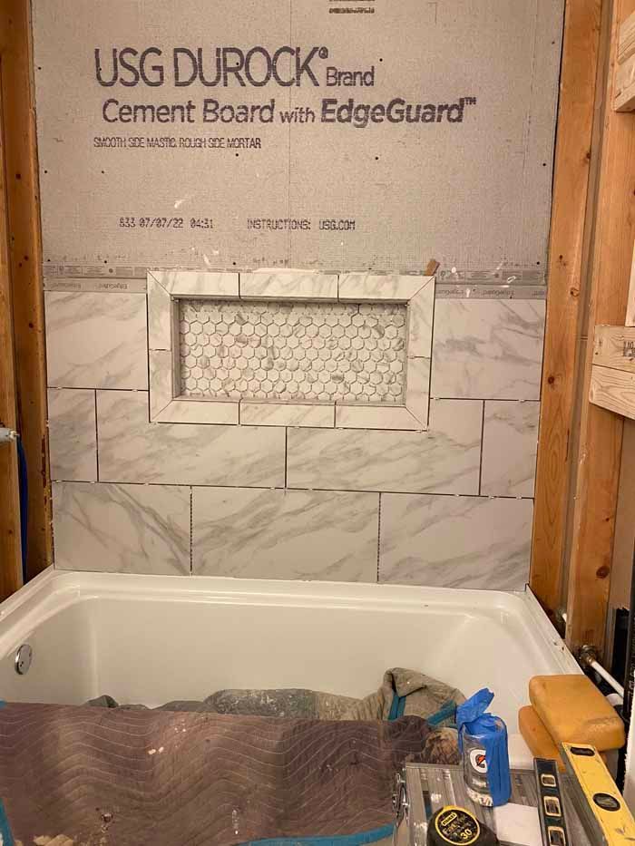 Bathtub under construction with cement board wall, tile pattern, and tools in a partially finished bathroom