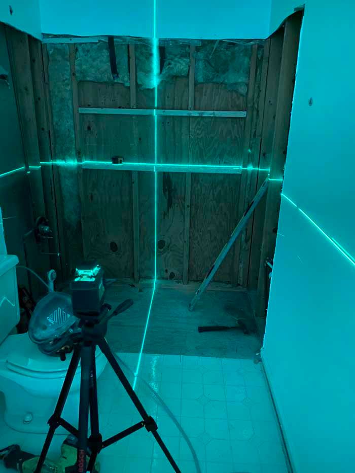 Blue-lit unfinished room with tripod and camera facing a wooden wall and closed doorway