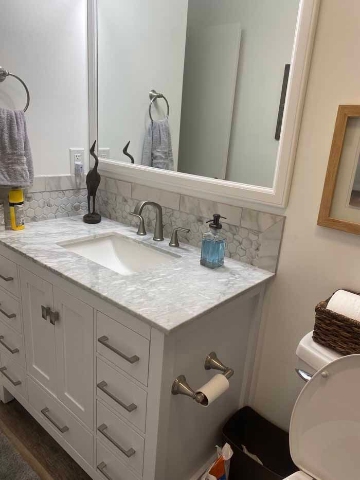 White bathroom vanity with marble counter, sink, mirror, soap dispenser, and towel rack