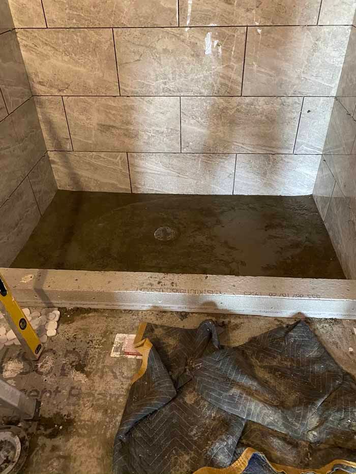 Partially tiled shower stall with a wet concrete floor and construction materials in the foreground