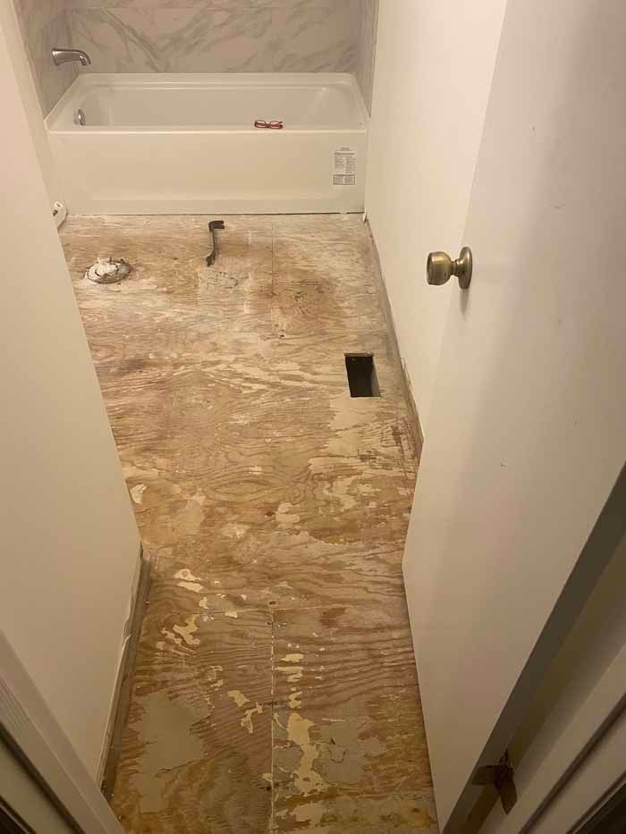 Damaged bathroom floor with exposed subfloor and a bathtub at the back