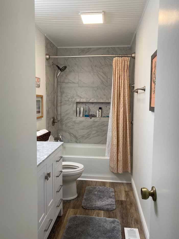 Small bathroom with toilet, sink, tub, and beige shower curtain in gray and white tones.