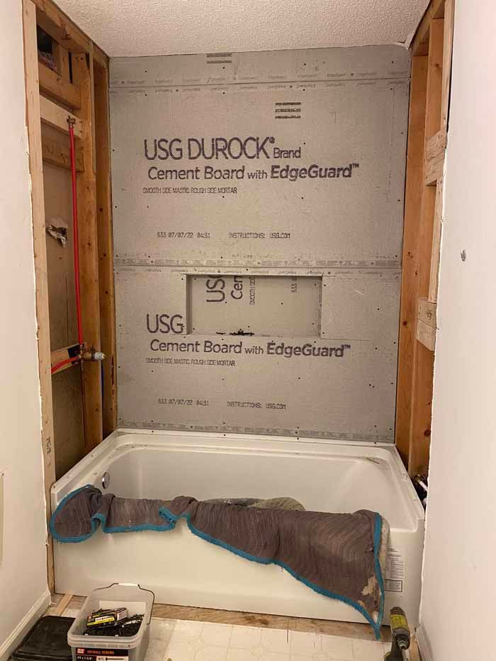Bathroom shower alcove under renovation with gray cement board, white tub, and construction materials on the floor