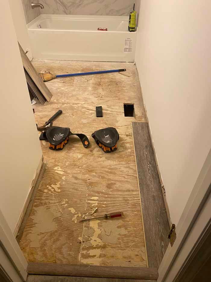 Small hallway under renovation with bare plywood floor, tools, and a bathtub at the end.