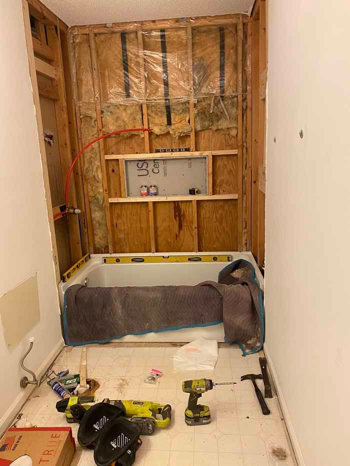 Partially renovated bathroom with exposed studs, a bathtub, and tools on the floor