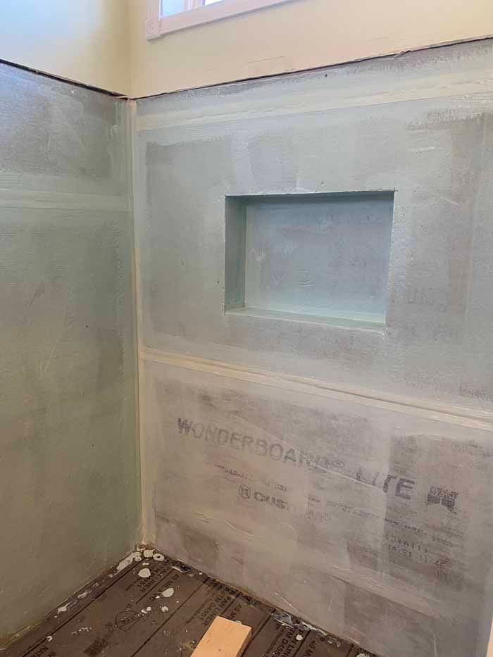 Bare unfinished bathroom wall with a small recessed niche and debris on the floor