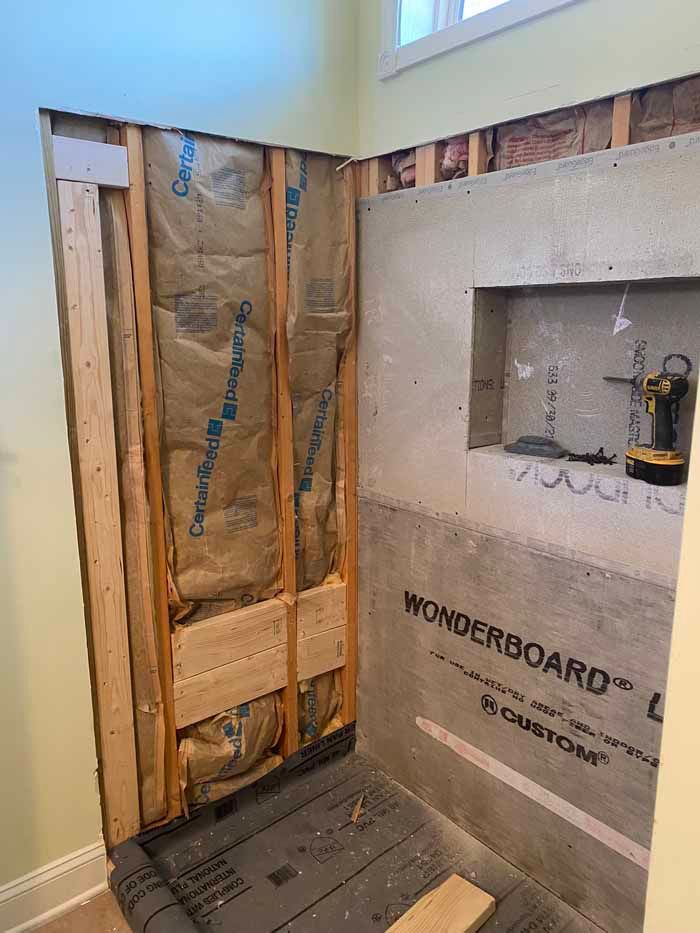 Bathroom wall under renovation with exposed studs, plumbing, and WonderBoard backing around a shower niche.