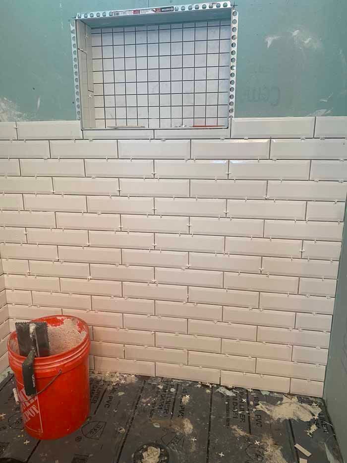 White brick wall with a small barred window above a red bucket and worn wooden floorboards
