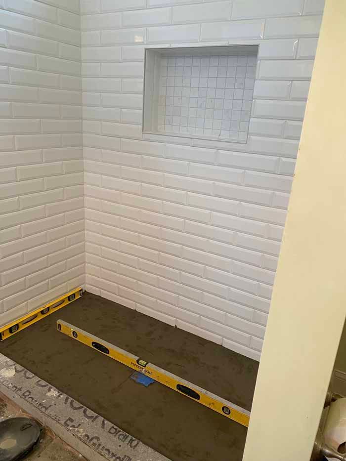 Empty tiled shower stall with a built-in niche and measuring tools on the floor.