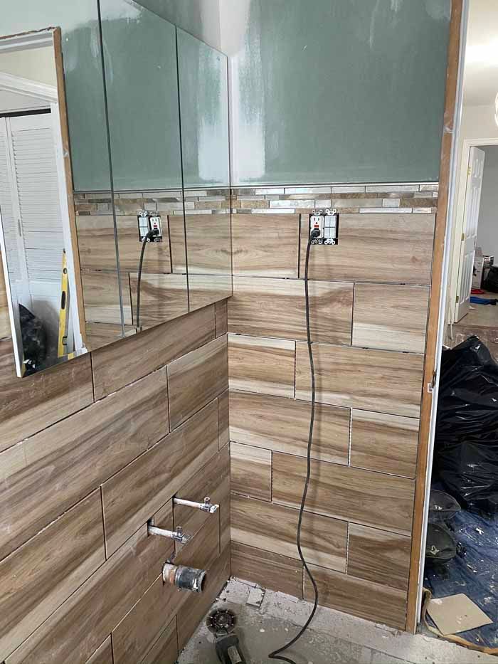 Modern bathroom vanity with wood paneling, mirror cabinets, sink, and glass shower doors