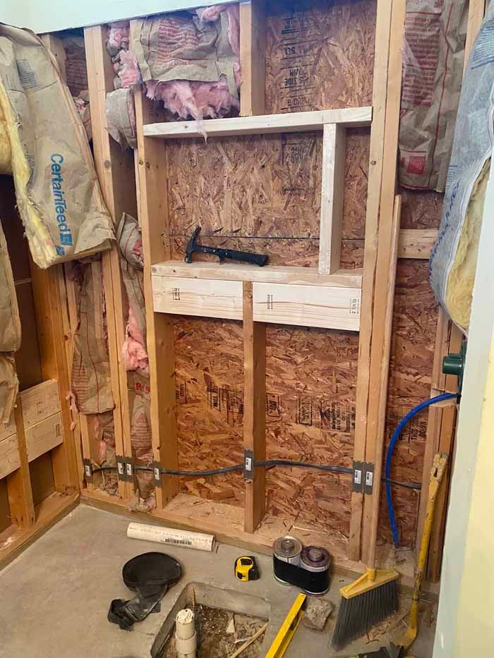 Exposed wall framing with insulation, tools on the floor, and a broom in an unfinished room.