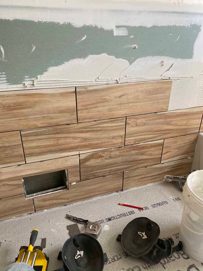 Bathroom wall with wood-look tile, unfinished drywall above, and tools on the floor during renovation