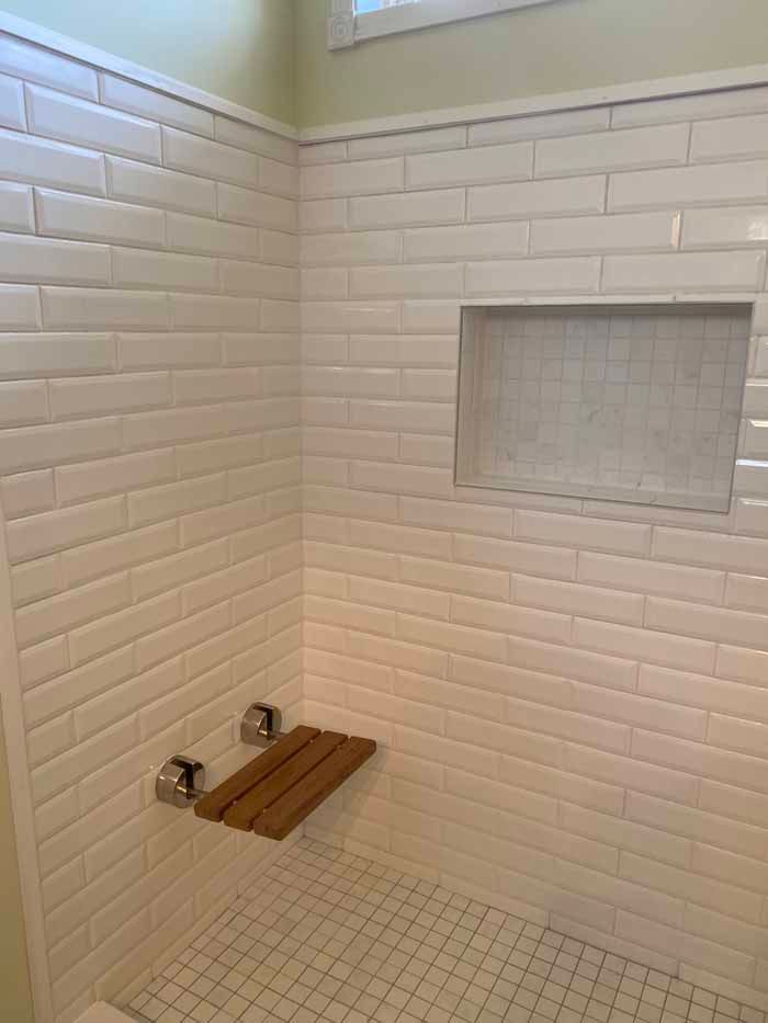 Small tiled shower with a wooden shower bench and built-in shelf niche.