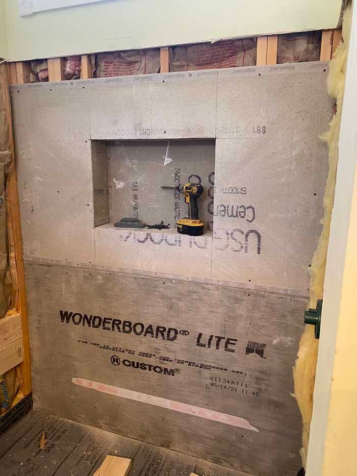 Bare drywall panel with a small cutout exposing plumbing, labeled WonderBoard Lite in a construction area