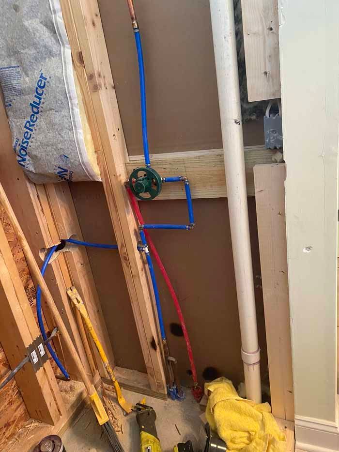 Exposed plumbing and pipes in an unfinished wall cavity with tools and insulation visible.