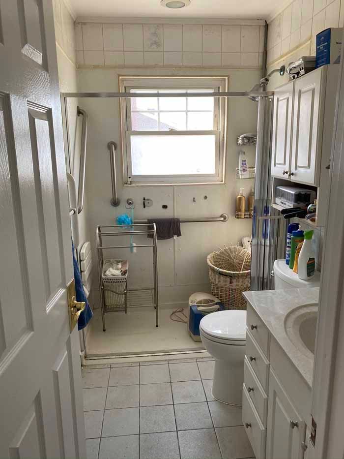Narrow white bathroom with a window, sink, toilet, cabinets, and tiled floor
