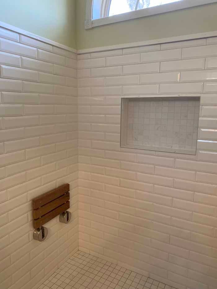 Tiled shower with built-in bench and recessed shelf under a small window