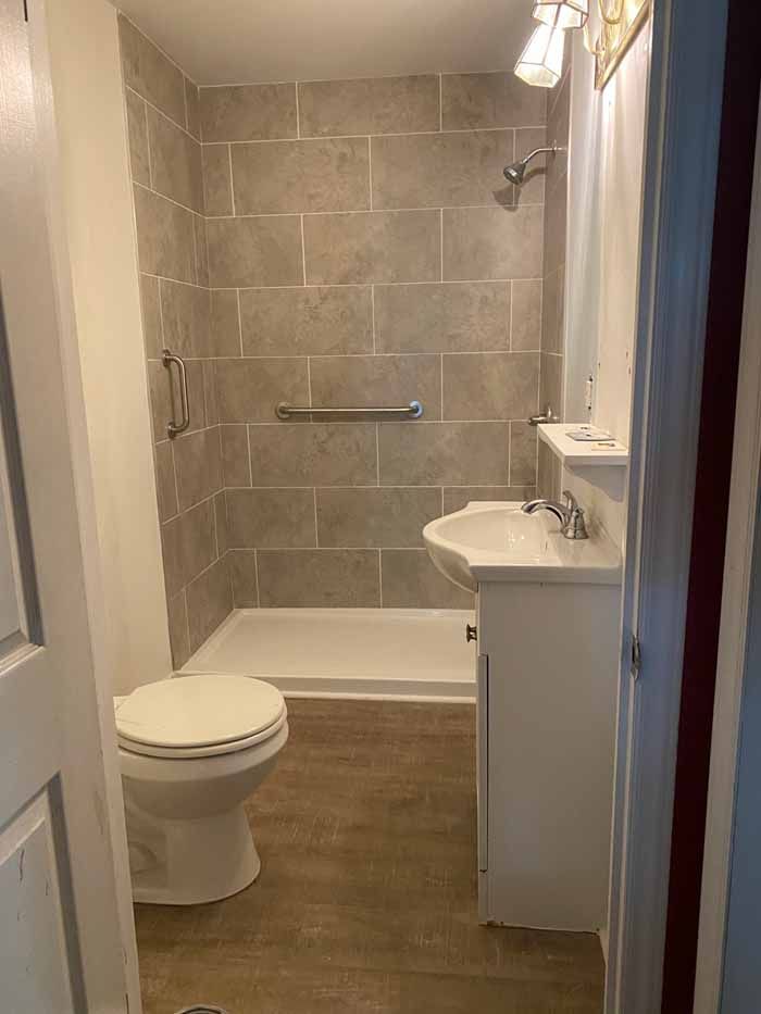 Compact bathroom with toilet, shower-tub, and white vanity on wood-look flooring.