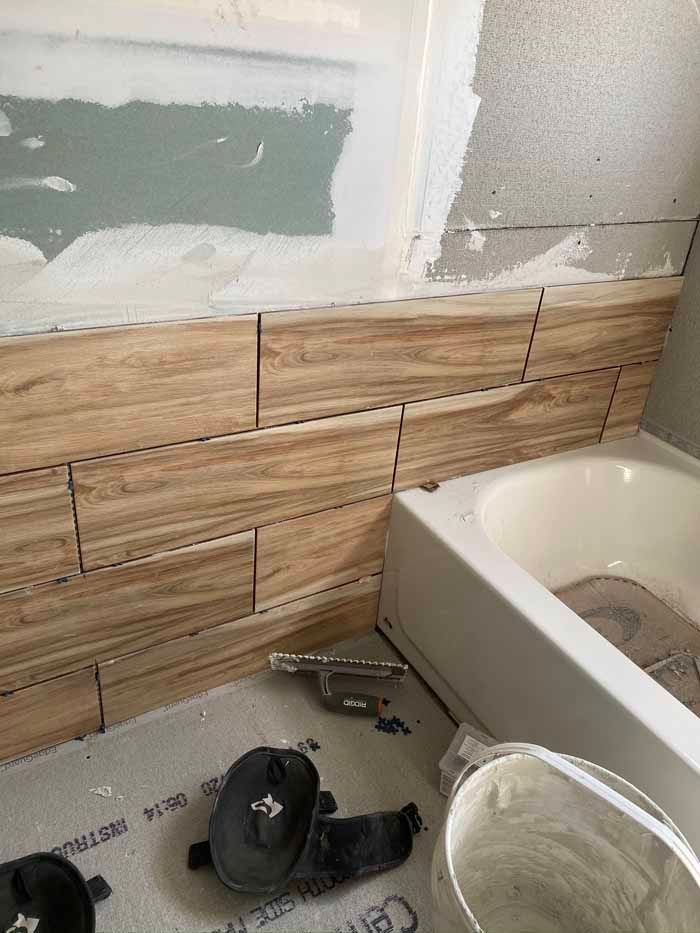 Bathroom renovation with wood-look tile half wall, tub edge, and tools on protective floor covering