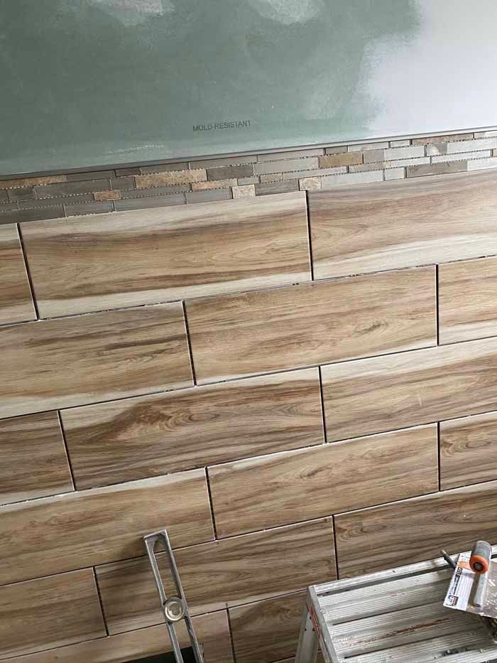 Wood-look tile wall with unfinished grout lines and a pale green painted upper wall area.