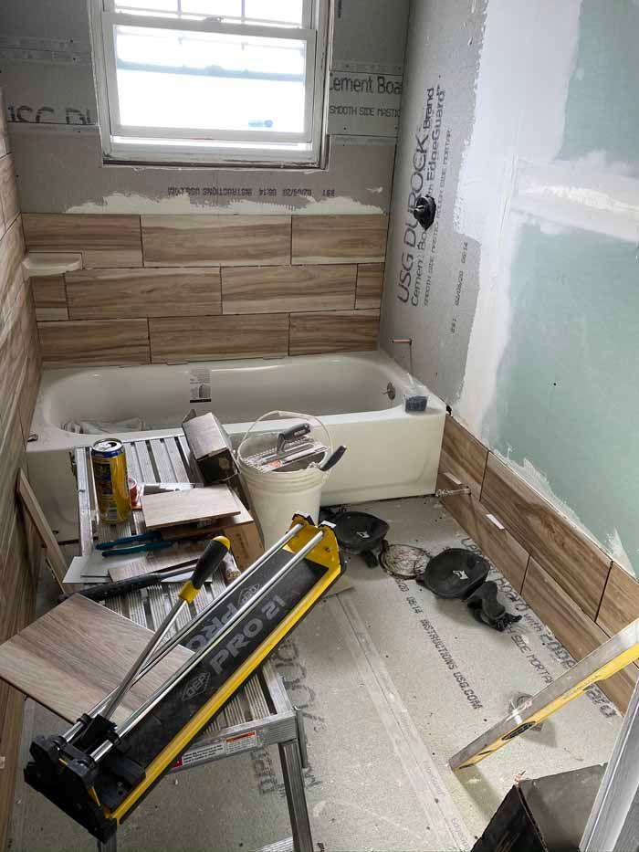 Bathroom renovation in progress, with tub, tile work, tools, and drywall patches.