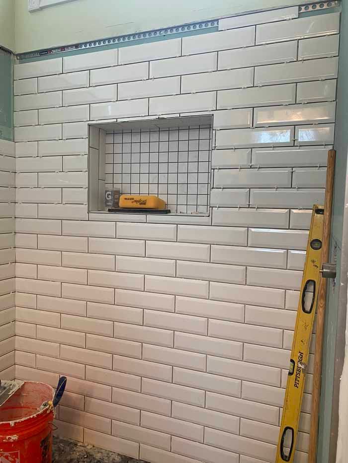 Tiled wall with a small recessed shelf under construction, featuring a level and ladder beside it.