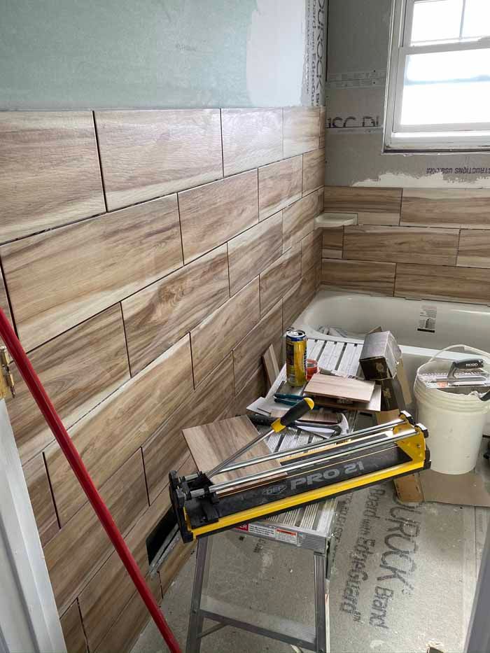 Tiled bathroom wall under renovation with tools, materials, and a ladder leaning nearby.