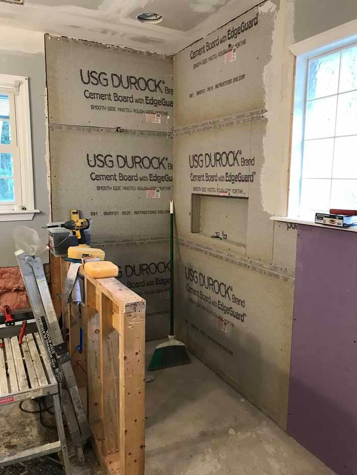 Bathroom under renovation with exposed green drywall, tools, and a window letting in daylight