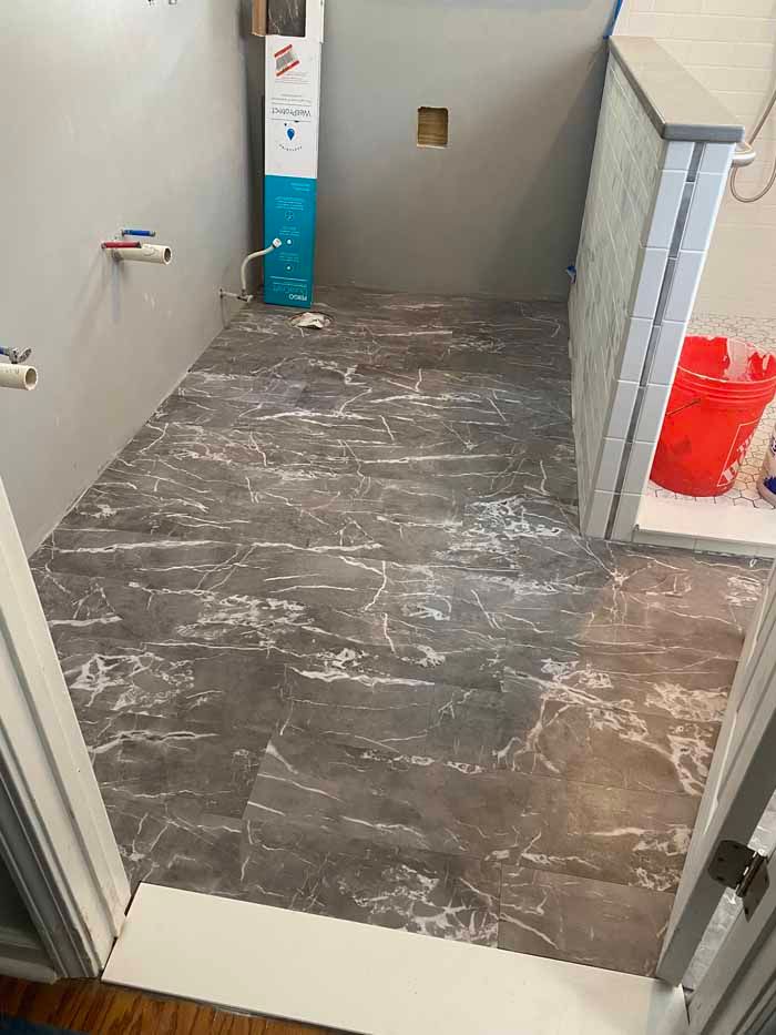 Partially tiled hallway under renovation, with exposed floor, tools, and a red bucket near the wall.