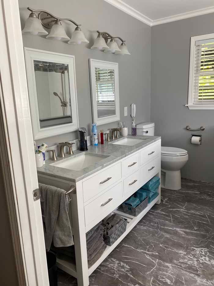 Modern gray bathroom with white vanity, double mirrors, and towels hanging on the side