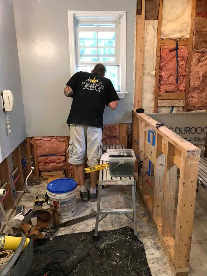 Person working at a window in a room under renovation, with exposed wall framing and tools nearby