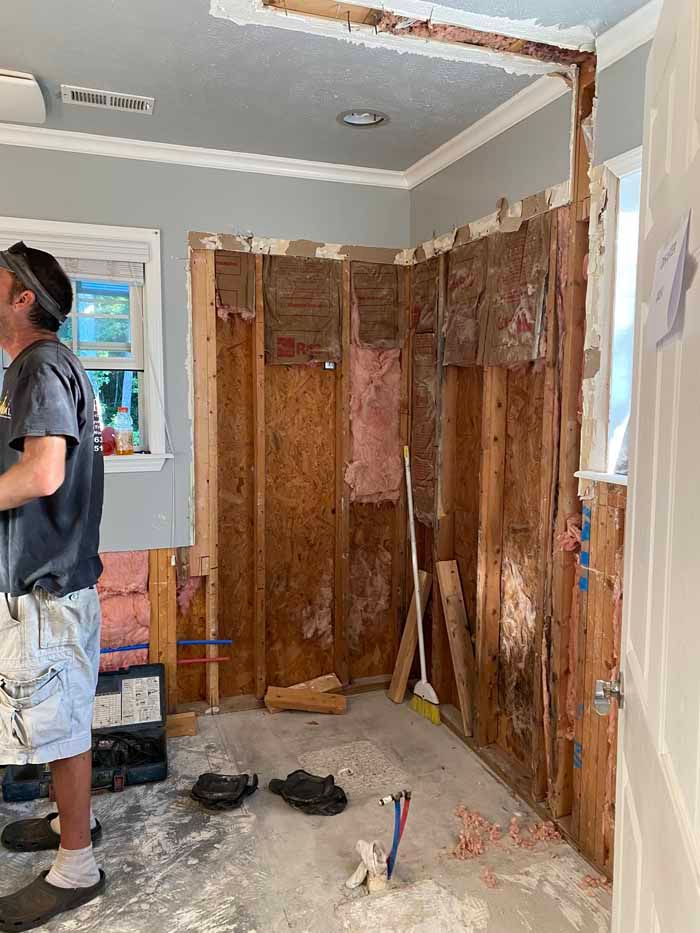 Partially demolished room with exposed studs, tools on the floor, and a worker standing at left